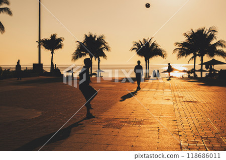 silhouettes of male players playing traditional football sepak takraw on promenade with palm trees by the sea in summer at sunrise in Asia silhouettes of male players playing traditional football sepak takraw on promenade with palm trees by the sea in summer at sunrise in Asia 118686011