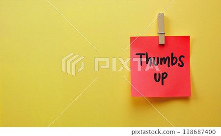 Thumbs up written on red sticky note hanging on yellow wall 118687400
