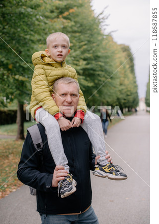 Dad holds on his son's shoulders. Beautiful family is spending time together outside. Dad and his little son are having fun on a roof terrace with view on a city. Sitting on father's shoulders and 118687855