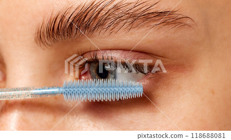 Close-up of a woman's eyelashes being brushed with wand, focusing on makeup application, and grooming against white studio background. 118688081