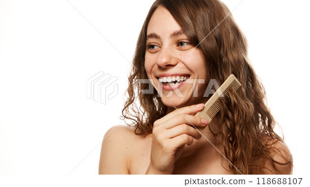 Smiling young woman combing her hair, showing joy in natural beauty and wellness moment against white studio background. 118688107