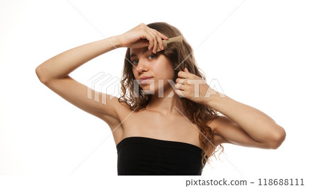 Woman combing her hair, representing beauty routine and hair care with focus on wellness against white studio background. 118688111