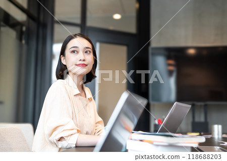 A woman with a calm expression looking at the view from the window in between working on her computer 118688203