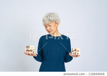 Senior woman comparing house models and having trouble deciding 118688608