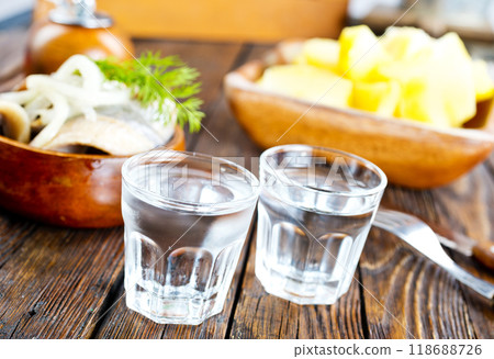 one empty second vodka-filled glass surrounded by a snack with herring and onions 118688726