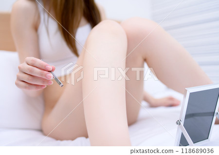 A young woman taking care of her crotch area, a delicate VIO zone, tweezing hair with tweezers while looking in the mirror 118689036