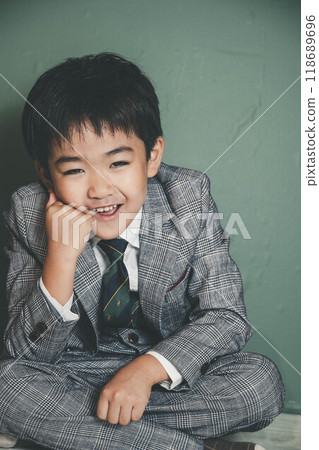 An innocent child in a suit sitting with his chin on his hands 118689696