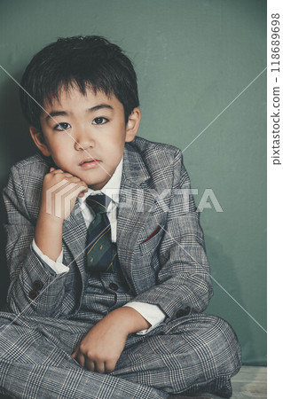An innocent child in a suit sitting with his chin on his hands 118689698