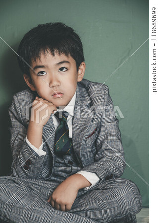 An innocent child in a suit sitting with his chin on his hands 118689699