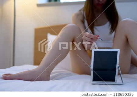 A young woman taking care of her VIO delicate zone groin area herself, tweezing hair with tweezers while looking in the mirror, dark cool colors 118690323