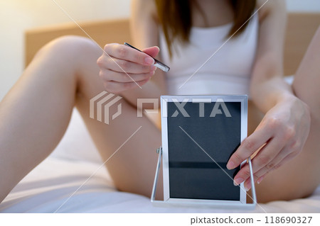 A young woman taking care of her VIO delicate zone groin area herself, tweezing hair with tweezers while looking in the mirror, dark cool colors A young woman taking care of her VIO delicate zone groin area herself, tweezing hair with tweezers while looking in the mirror, dark cool colors 118690327