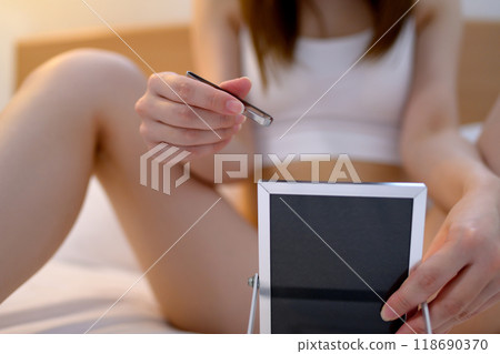 A young woman doing self-care for her VIO delicate zone groin area, tweezing hair with tweezers while looking in the mirror, negative dark A young woman doing self-care for her VIO delicate zone groin area, tweezing hair with tweezers while looking in the mirror, negative dark 118690370