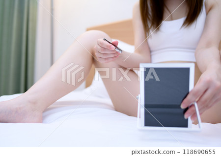 VIO精緻區 一位年輕女子在自我照顧自己的胯部，一邊照鏡子一邊用鑷子拔出鑷子，日光白色 118690655
