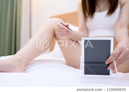 A young woman taking care of her VIO delicate zone crotch area herself, tweezing hair with tweezers while looking in the mirror, real color 118690656