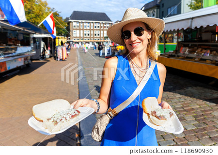 Portrait young happy adult female tourist woman enjoy eating traditional Dutch sandwich with pickled matjes herring onion at local market in Groningen Netherlands. Holland tourism travel destination 118690930