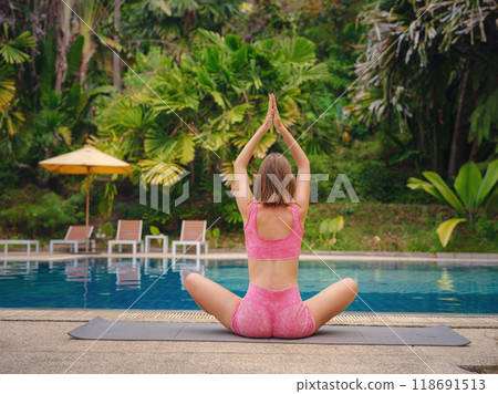 woman doing stretching exercising for body feeling inspiration for slimming, sportive female enjoying yoga practice during morning workout at nature with greenery at pool 118691513