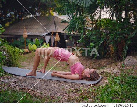 Beautiful woman practices yoga by pool in morning in Thailand. Young female in sportswear in hotel exotic garden. perfect flexible body recreating doing yoga poses feeling inner peace and vitality Beautiful woman practices yoga by pool in morning in Thailand. Young female in sportswear in hotel exotic garden. perfect flexible body recreating doing yoga poses feeling inner peace and vitality 118691515