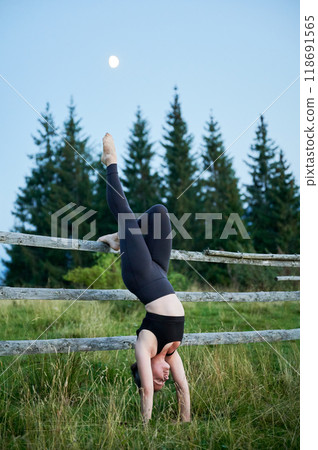 Woman practicing yoga outdoors in the mountains in a serene, natural setting. Female performing yoga pose, with backdrop of beautiful mountain landscape at sunrise or sunset. 118691565