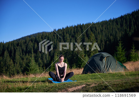 Woman practicing yoga and meditating outdoors in the mountains in a serene, natural setting. Female performing yoga pose on mat. Woman practicing yoga and meditating outdoors in the mountains in a serene, natural setting. Female performing yoga pose on mat. 118691569