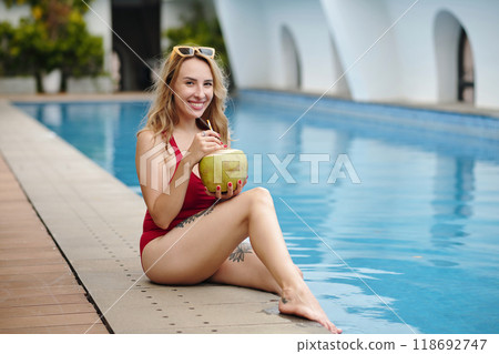Smiling Woman Relaxing by Poolside Holding Coconut Drink Smiling Woman Relaxing by Poolside Holding Coconut Drink 118692747