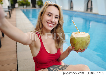 Smiling Woman Taking Selfie by Pool Holding Coconut Drink Smiling Woman Taking Selfie by Pool Holding Coconut Drink 118692748