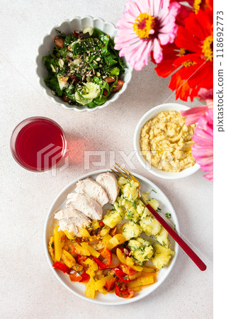 A balanced meal of boiled potatoes with baked vegetables and chicken breast, paired with a fresh tomato and cucumber salad topped with seeds, and a refreshing raspberry compote 118692773