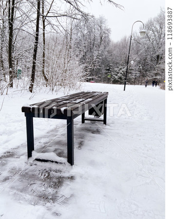 Solitary bench stands in a snow covered park during winter, inviting quiet reflection and peace. Winter landscape captures the beauty of cold season in nature Solitary bench stands in a snow covered park during winter, inviting quiet reflection and peace. Winter landscape captures the beauty of cold season in nature 118693887