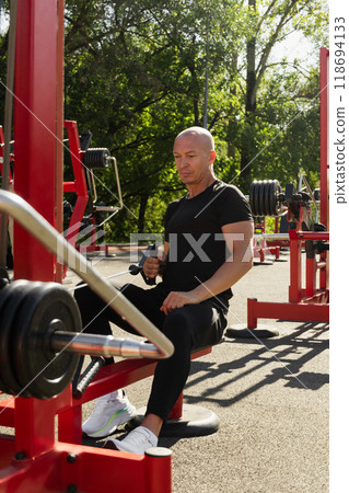 Lat rowing exercises. Adult man training at public gym park. Outdoors activity. Fitness coach show exercise for back. 118694133