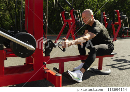 Lat rowing exercises. Adult man training at public gym park. Outdoors activity. Fitness coach show exercise for back. 118694134