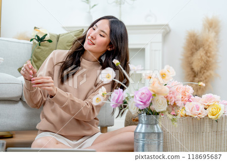Pretty Asian woman sit on the floor and hold the flower during do flower arrangement in living room of her house with relax time. 118695687