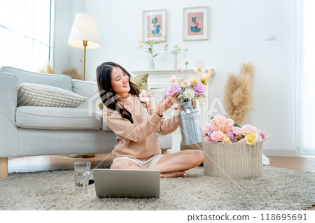 Side view of pretty Asian woman sit on the floor and happiness with flower arrangement in living room of her house with relax time. 118695691