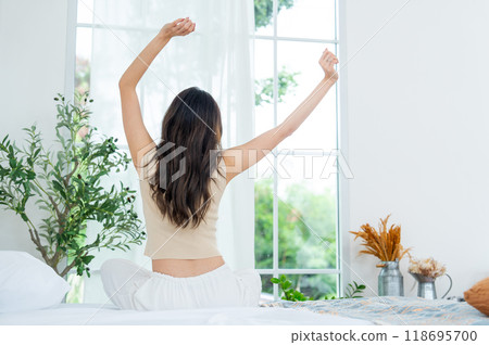 Back of young beautiful Asian woman wake up and stretch oneself on bed in the morning with happiness. Back of young beautiful Asian woman wake up and stretch oneself on bed in the morning with happiness. 118695700