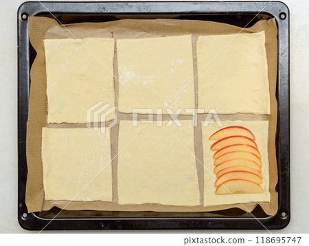 Puff pastry squares with apple slices on a baking tray. Puff pastry squares with apple slices on a baking tray. 118695747