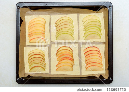 Sliced apple pieces arranged on puff pastry sheets on a baking tray. 118695750