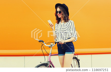 Summer colorful portrait of happy smiling young woman with smartphone, bicycle on orange background 118697251