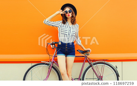 Summer colorful portrait of beautiful young woman with bicycle blowing kiss on orange background 118697259