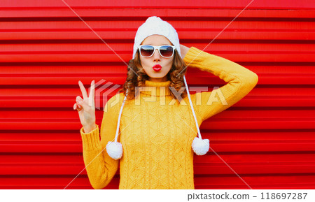 Fashion woman blowing red lips wearing colorful knitted yellow sweater hat over red background Fashion woman blowing red lips wearing colorful knitted yellow sweater hat over red background 118697287