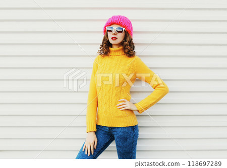 Fashion young woman model wearing a knitted pink hat, yellow colorful sweater over white background 118697289