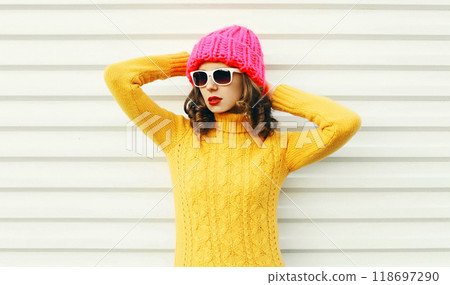 Fashion young woman wearing a knitted pink hat, yellow colorful sweater over white background 118697290