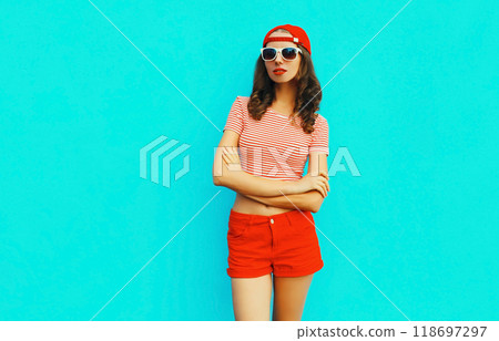 Summer portrait of young woman wearing baseball cap, red shorts on blue background Summer portrait of young woman wearing baseball cap, red shorts on blue background 118697297
