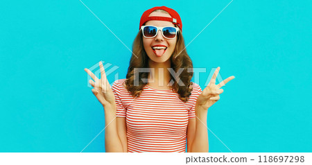 Portrait of happy cheerful young woman showing her tongue in red baseball cap on blue background Portrait of happy cheerful young woman showing her tongue in red baseball cap on blue background 118697298