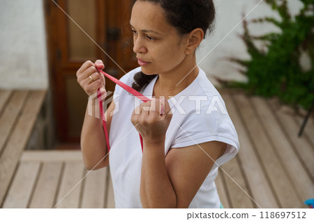 Woman exercising with resistance band on wooden deck for outdoor home workout and fitness routine 118697512