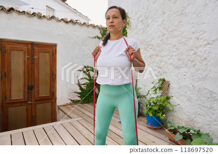 Woman exercising with resistance band outdoors on a wooden deck in casual fitness attire 118697520