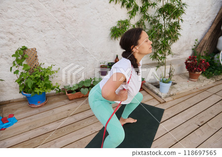 Woman practicing yoga with a resistance band on a wooden deck surrounded by potted plants Woman practicing yoga with a resistance band on a wooden deck surrounded by potted plants 118697565