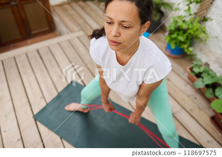 Woman practicing resistance band workout on wooden deck for home fitness and exercise routine 118697575