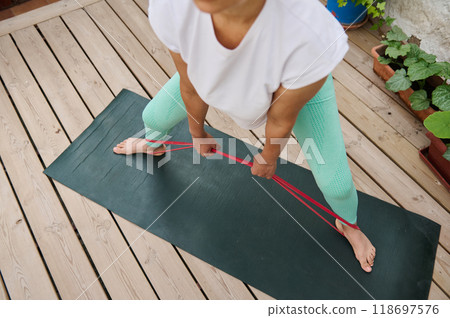 Woman practicing resistance band exercise on yoga mat outdoors for strength and flexibility training 118697576
