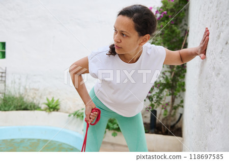 Woman practicing fitness exercises with a resistance band in an outdoor garden setting wearing comfortable workout attire Woman practicing fitness exercises with a resistance band in an outdoor garden setting wearing comfortable workout attire 118697585