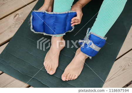 Woman preparing for exercise with ankle weights on yoga mat for fitness routine outdoors 118697594