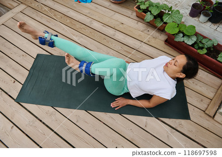 Woman practicing yoga on a wooden deck with ankle weights focusing on core strength and balance outdoors Woman practicing yoga on a wooden deck with ankle weights focusing on core strength and balance outdoors 118697598