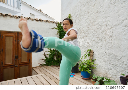 Woman practicing a powerful side kick with ankle weights on a wooden deck 118697607